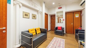 A hotel lobby with a black leather sofa, a patterned rug, and a wooden floor. - Andenis Tiber House  (Rome)