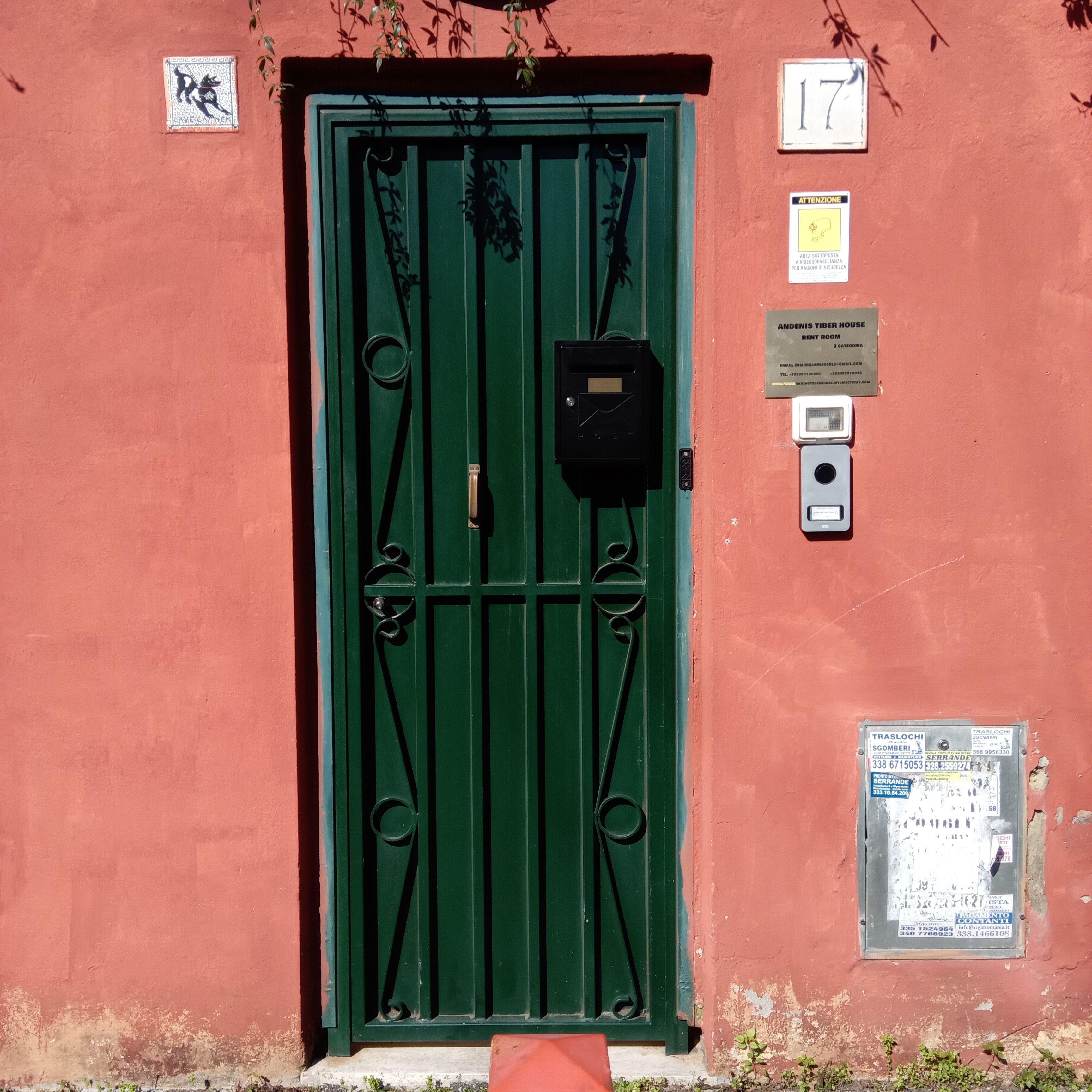 A green door with a metal gate, a number plate, and a sign indicating Andeni Timber House Room 2 Category.