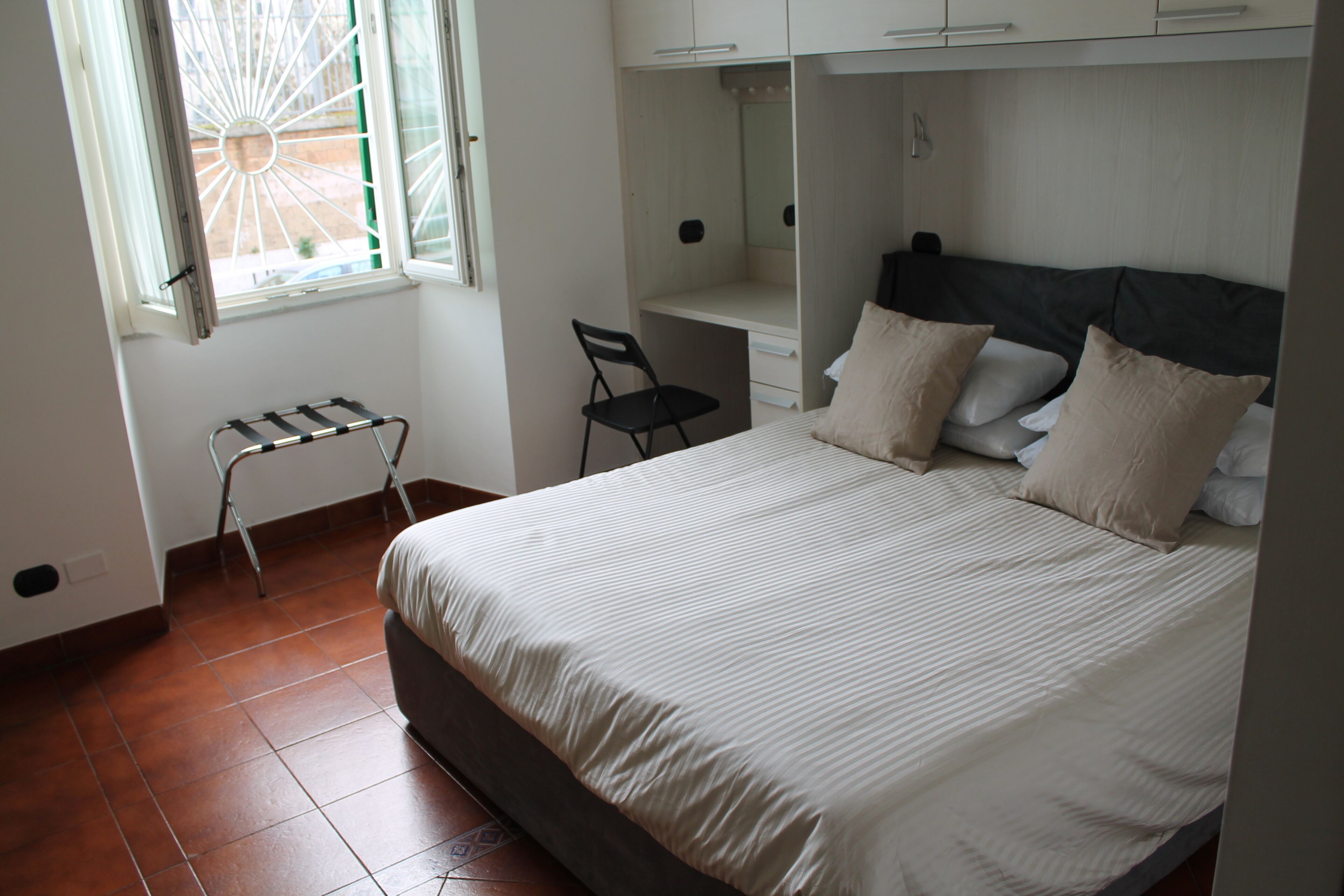 A bedroom with a bed, a chair, a small table, and a wardrobe.