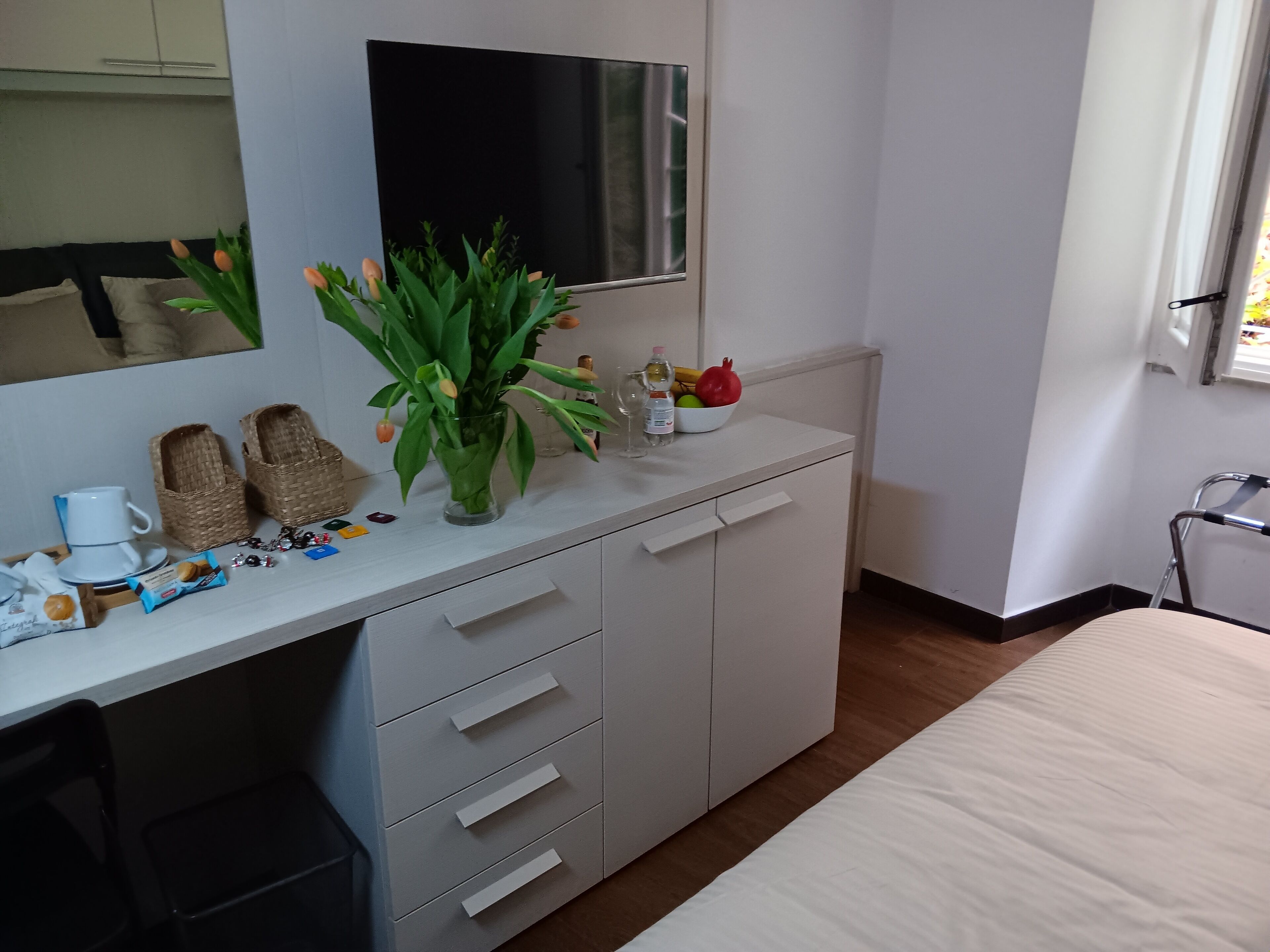 A bedroom with a bed, a dresser with drawers, a mirror, a television, and a window.