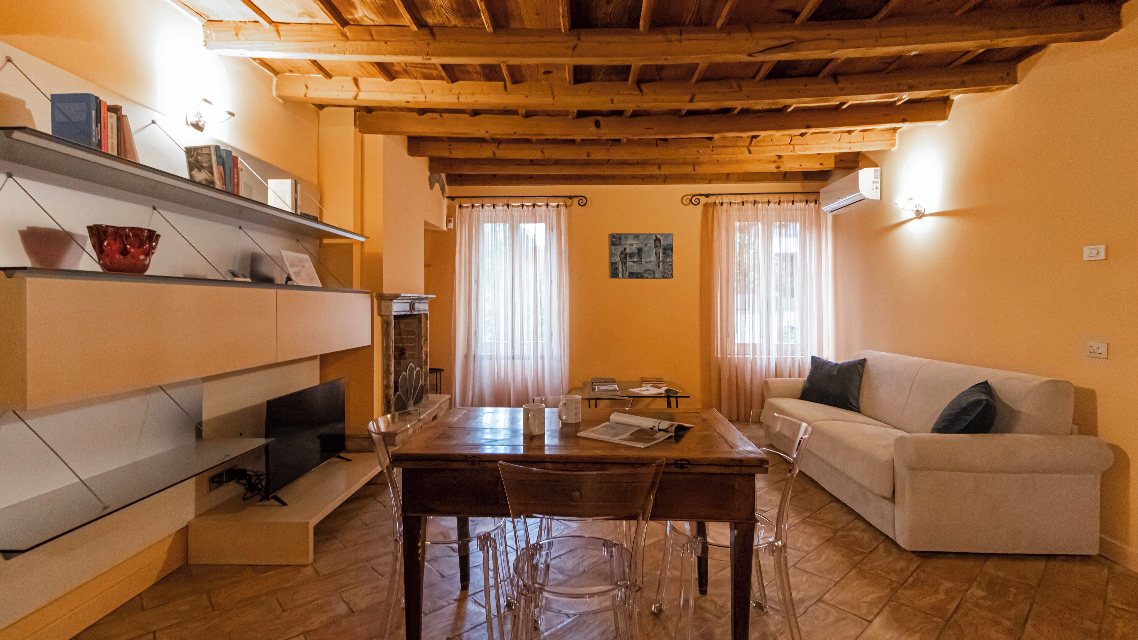 Ein Wohnzimmer mit Holzboden, einer Couch, einem Esstisch mit Stühlen und einem Kamin.