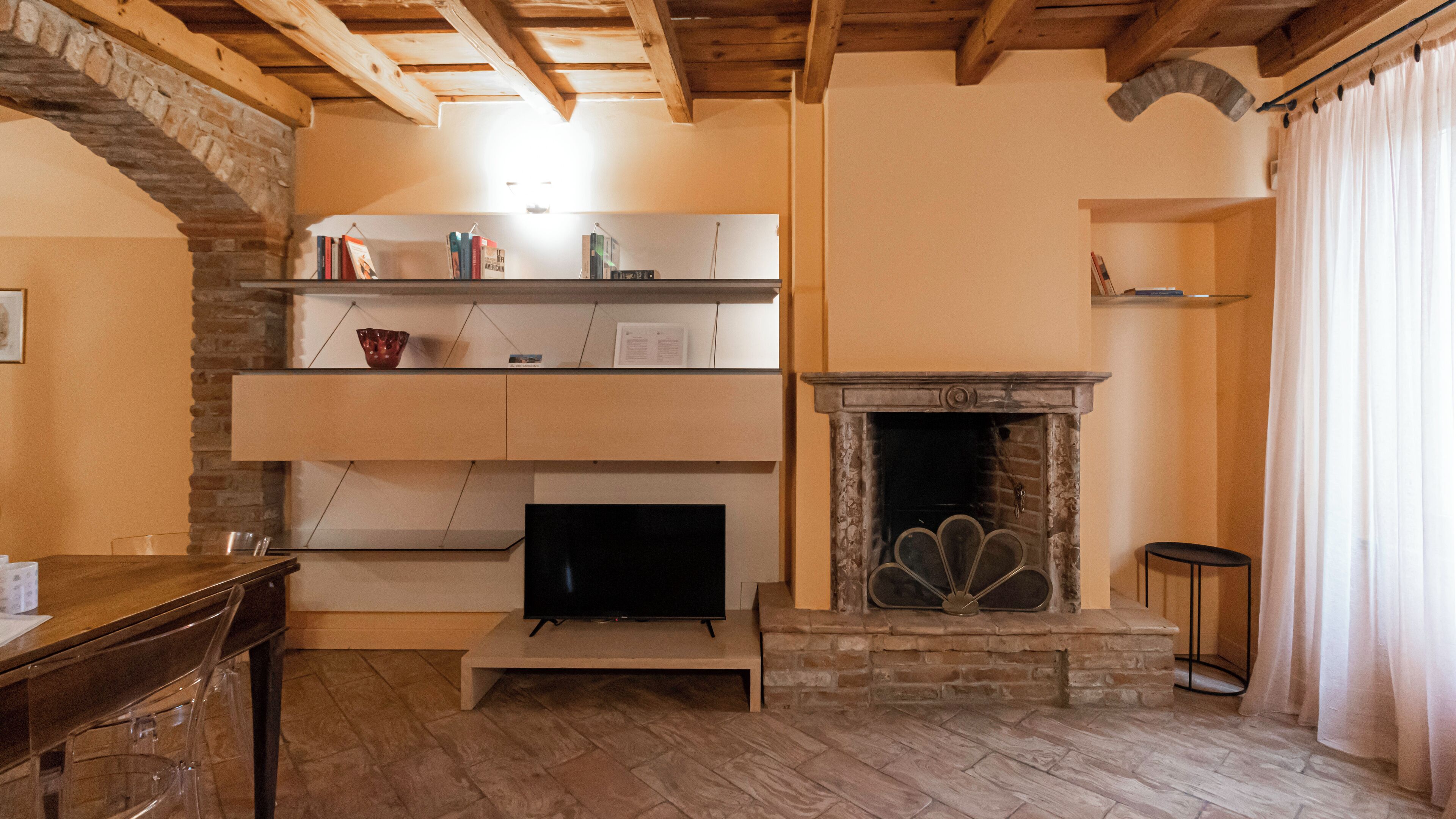 A cozy living room with a fireplace, wooden beams, a TV, and a bookshelf.