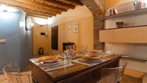 A dining area with a wooden island table set for four, surrounded by chairs. There are plates, glasses, and cutlery on the table. The room has a stone wall and a wooden ceiling. - Italianway Easy - Garibaldi 93 B (Milan)