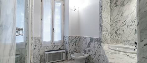 A bathroom with a marble floor, a bidet, a sink, and a window with curtains.