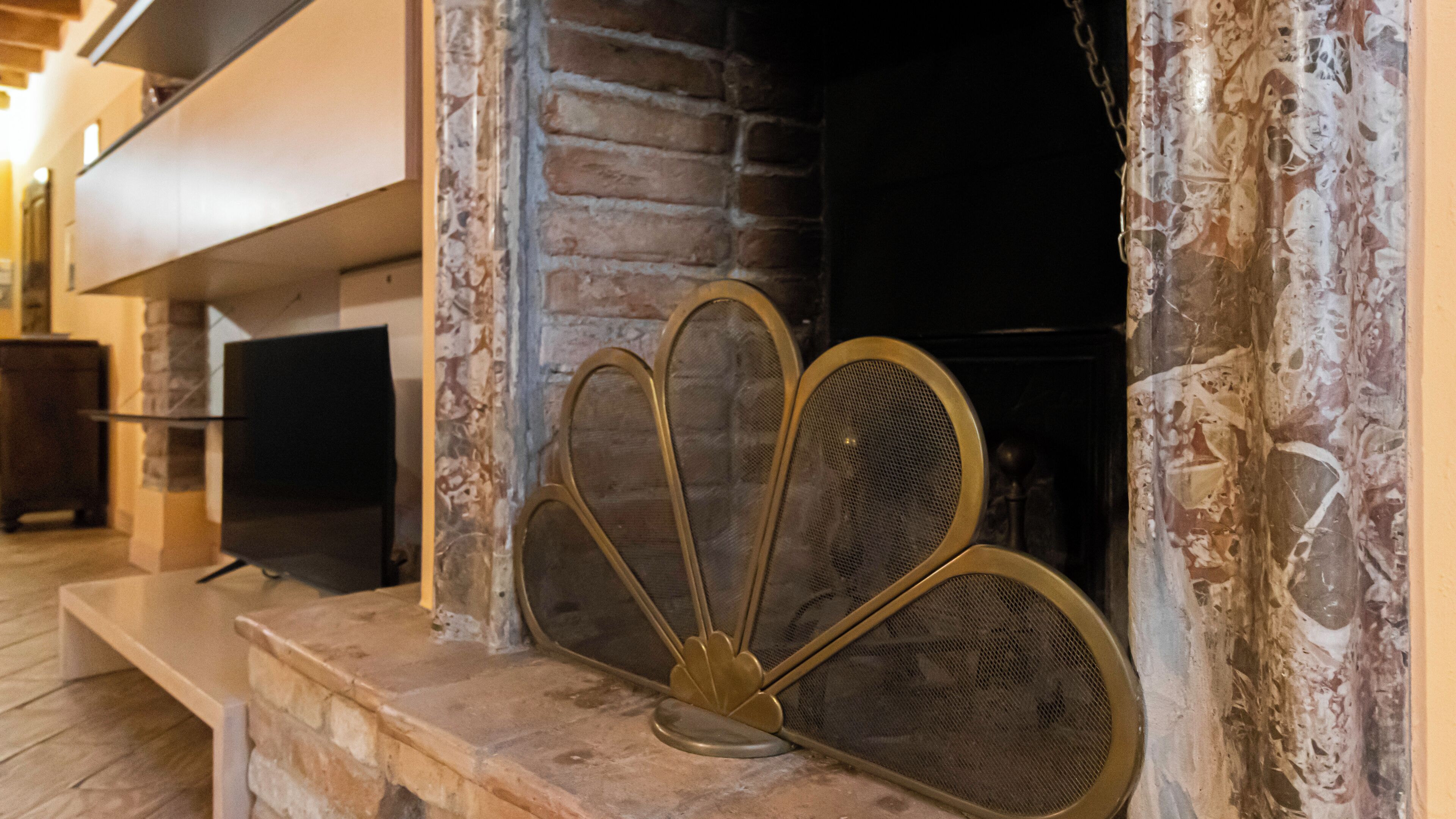 A stone fireplace with a metal screen, a television on a stand to the left, and a stone wall.