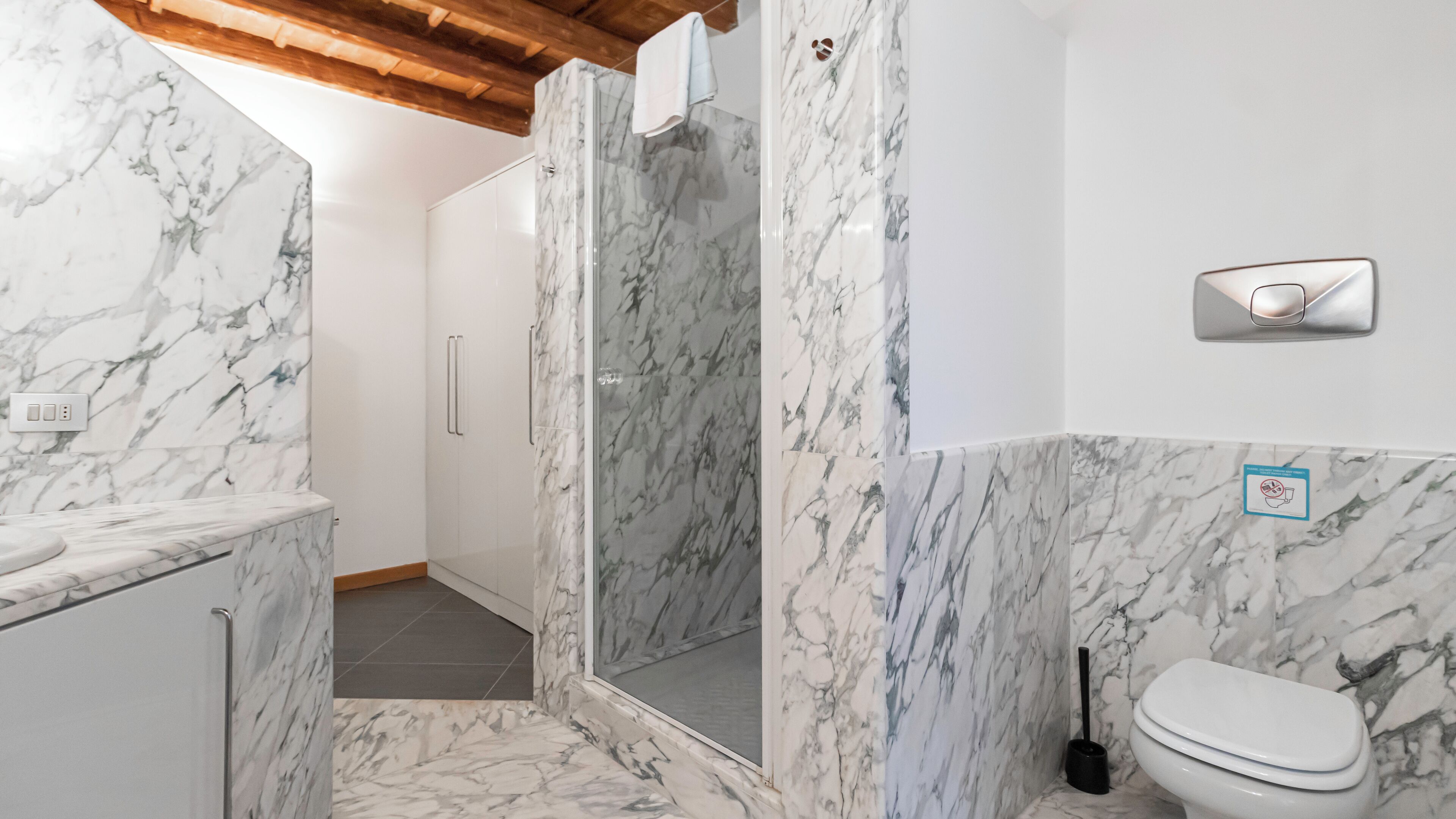 A bathroom with marble walls, a shower enclosure, a toilet, and a bidet.