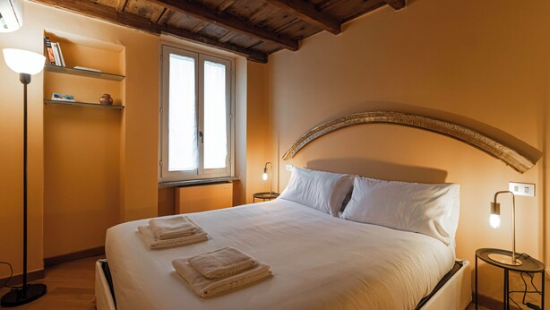 A neatly made bed with folded towels, a bedside lamp, and a shelf with books. - Italianway Easy - Garibaldi 93 B (Milan)