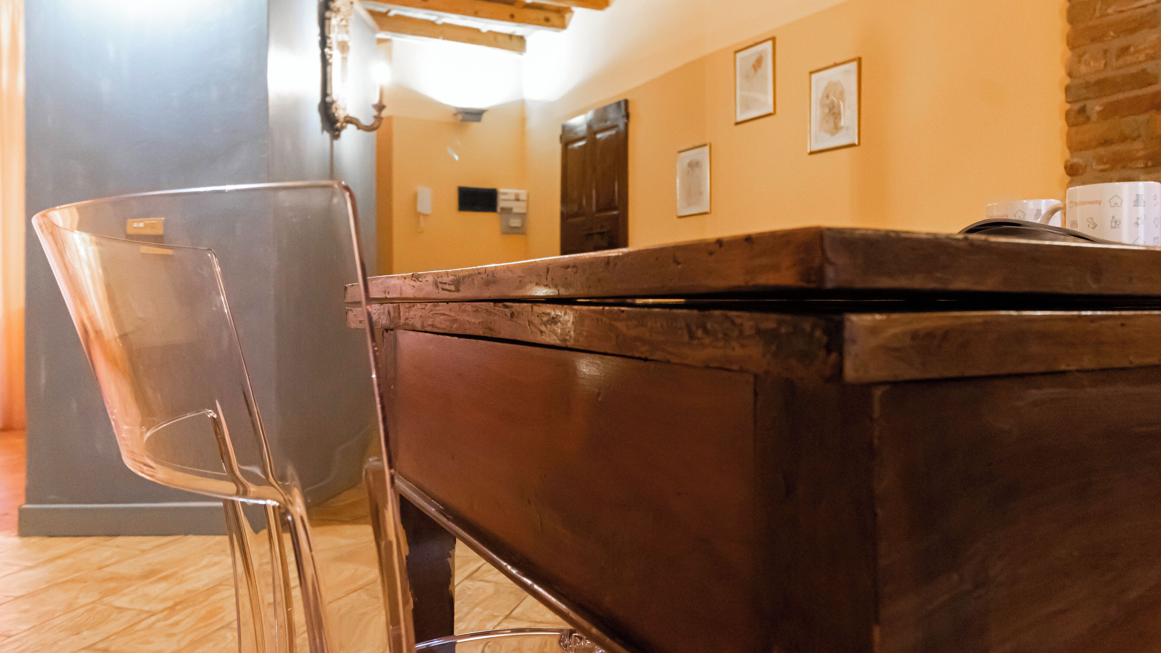 A wooden table with a metal frame, a clear plastic chair, and a wall with framed pictures.