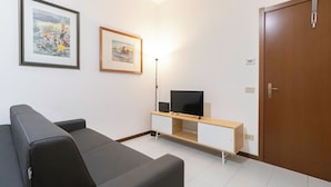 Ein modernes Wohnzimmer mit einer schwarzen Couch, einem Flachbildfernseher auf einem Holzboden und zwei gerahmten Kunstwerken an der Wand.