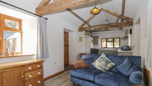 A cozy living room with a blue sofa, wooden cabinet, and a kitchen in the background. - Keepers Barn (Worcester)