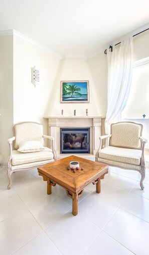 Een kamer met een open haard, twee fauteuils, een salontafel en een schilderij van een strand.