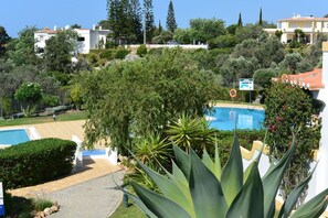 Área de piscina com posto de salva-vidas, cercada por vegetação exuberante e céu claro.