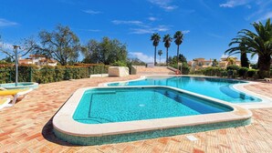 A swimming pool with a tiled edge, surrounded by a brick patio, palm trees, and a clear blue sky. - 61B  Apartment in the Heart of Gramacho Gof Complexo (Estômbar)