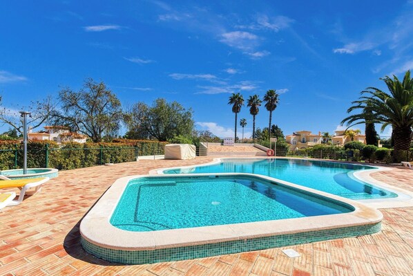 A swimming pool with a tiled edge, surrounded by a brick patio, palm trees, and a clear blue sky.