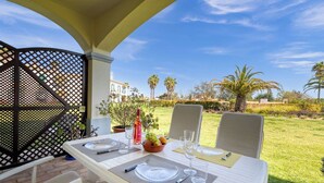 A dining table set outdoors with a view of a well-maintained garden and palm trees. - 61B  Apartment in the Heart of Gramacho Gof Complexo (Estômbar)