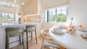 Une cuisine moderne avec un coin repas, comprenant un îlot central, des tabourets de bar et une vue dégagée grâce à de grandes fenêtres.