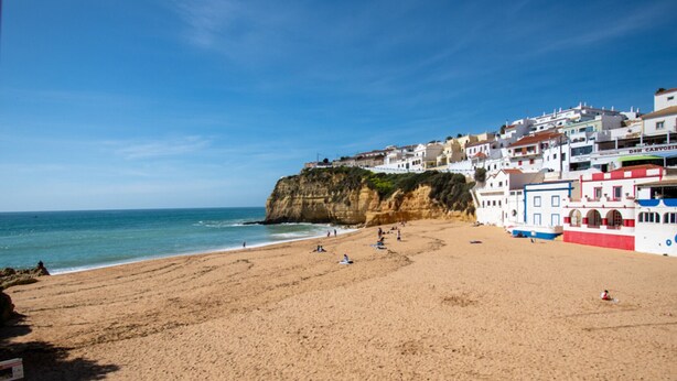 Une plage côtière avec des bâtiments situés sur une falaise, un ciel dégagé et une rive sablonneuse.