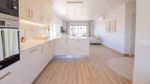 Une cuisine moderne avec des meubles blancs, un four encastré et un îlot central doté d’un évier.