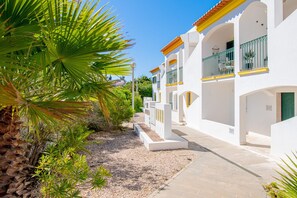A white building with balconies, a gravel pathway, and a palm tree.
