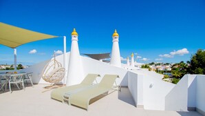 Une terrasse sur le toit avec des murs blancs, deux phares, un fauteuil suspendu et une table avec des chaises.