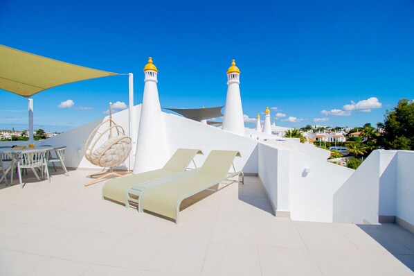 A rooftop terrace with white walls, two lighthouses, a hanging chair, and a table with chairs.