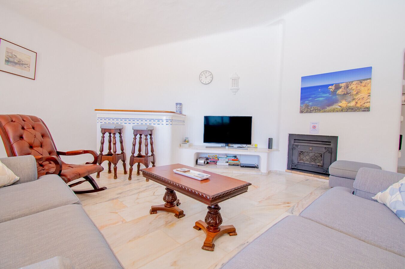 Een woonkamer met een televisie, een open haard en een schilderij van een kustlandschap.