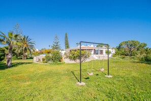 A house with a garden, a swing set, and a clear blue sky.