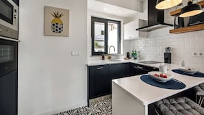 Een moderne keuken met zwarte kastjes, witte aanrechtbladen en een centraal eiland met een schaal fruit.
