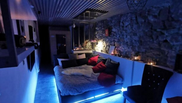 Un dormitorio moderno con una pared de piedra, una cama con iluminación azul debajo y una mesita de noche con velas.