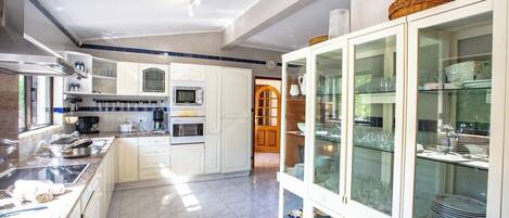 A modern kitchen with white cabinetry, a built-in microwave, and a glass-fronted display cabinet.