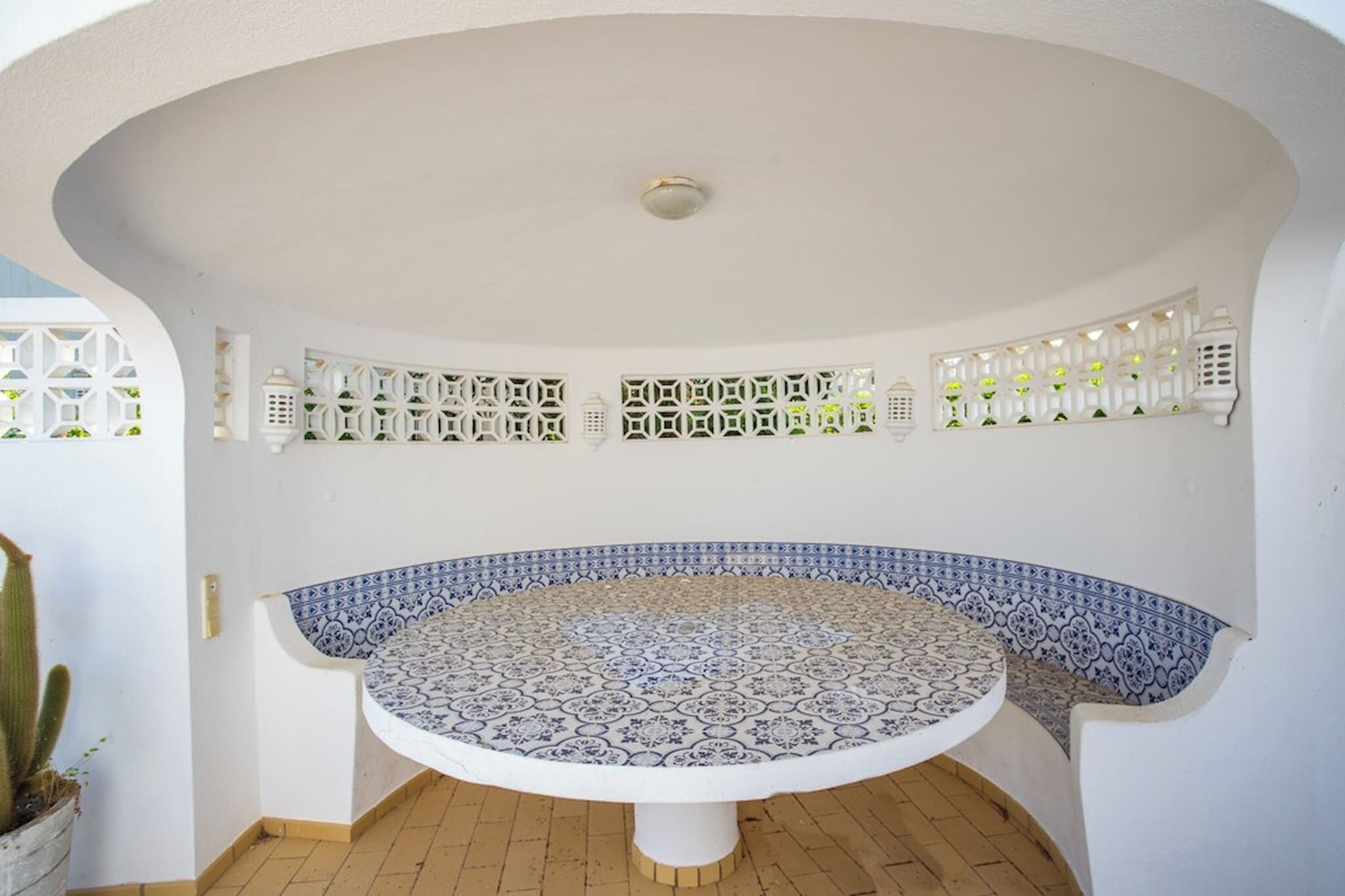 A circular tiled table with a white pedestal base, surrounded by white walls with decorative lattice patterns and white lanterns.