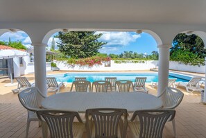 Relax by the pool surrounded by lush greenery and a clear sky.