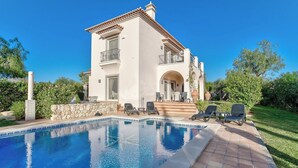A two-story house with a swimming pool, outdoor seating, and a stone wall.
