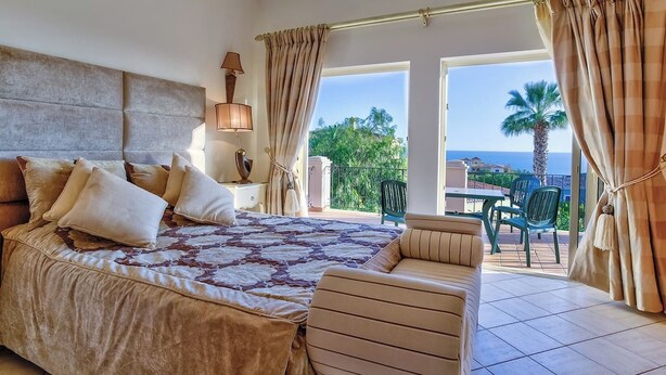 A bedroom with a large bed, a nightstand, a lamp, and a view of the outdoors.