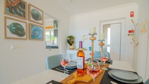 Spiseområde med et bord dækket til to personer, inklusiv vinflaske, glas og tallerkener.