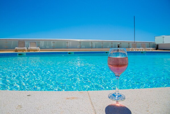A swimming pool with lounge chairs and a glass of pink drink on the edge.