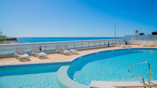 En pool med klart, blåt vand, omgivet af liggestole og et gelænder af glas med udsigt over havet.