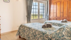 Une chambre avec deux lits, une fenêtre avec des rideaux, une armoire en bois et un luminaire fixé au mur.