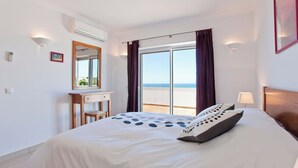 Habitación de hotel con cama, escritorio, silla, ventana con cortinas y vista al mar.
