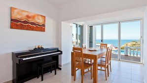 Un comedor con piano, una mesa y sillas, con vistas a un paisaje marino.