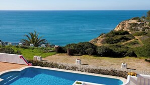 Una piscina con vistas al mar, rodeada de vegetación y un paisaje rocoso.