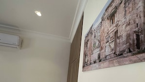 A bedroom with a bed, bedside table with a lamp, an air conditioning unit, a painting on the wall, and a wooden wardrobe. - Antica Jabalal-lwebdeh (Amman)