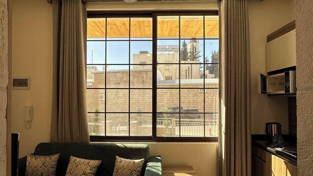 A room with a sofa, a window with curtains, a ceiling light fixture, and a kitchen area with a microwave. - Antica Jabalal-lwebdeh (Amman)