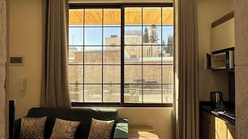 A room with a sofa, a window with curtains, a ceiling light fixture, and a kitchen area with a microwave.