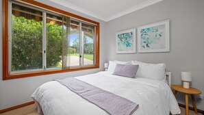 Ein Schlafzimmer mit großem Fenster, einem Bett mit weißer Bettwäsche, zwei Wandleuchten und zwei gerahmten Kunstwerken.