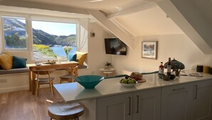 Uma cozinha moderna com uma ilha grande, um espaço de refeições com vista para o mar, e uma área de estar aconchegante junto à janela.
