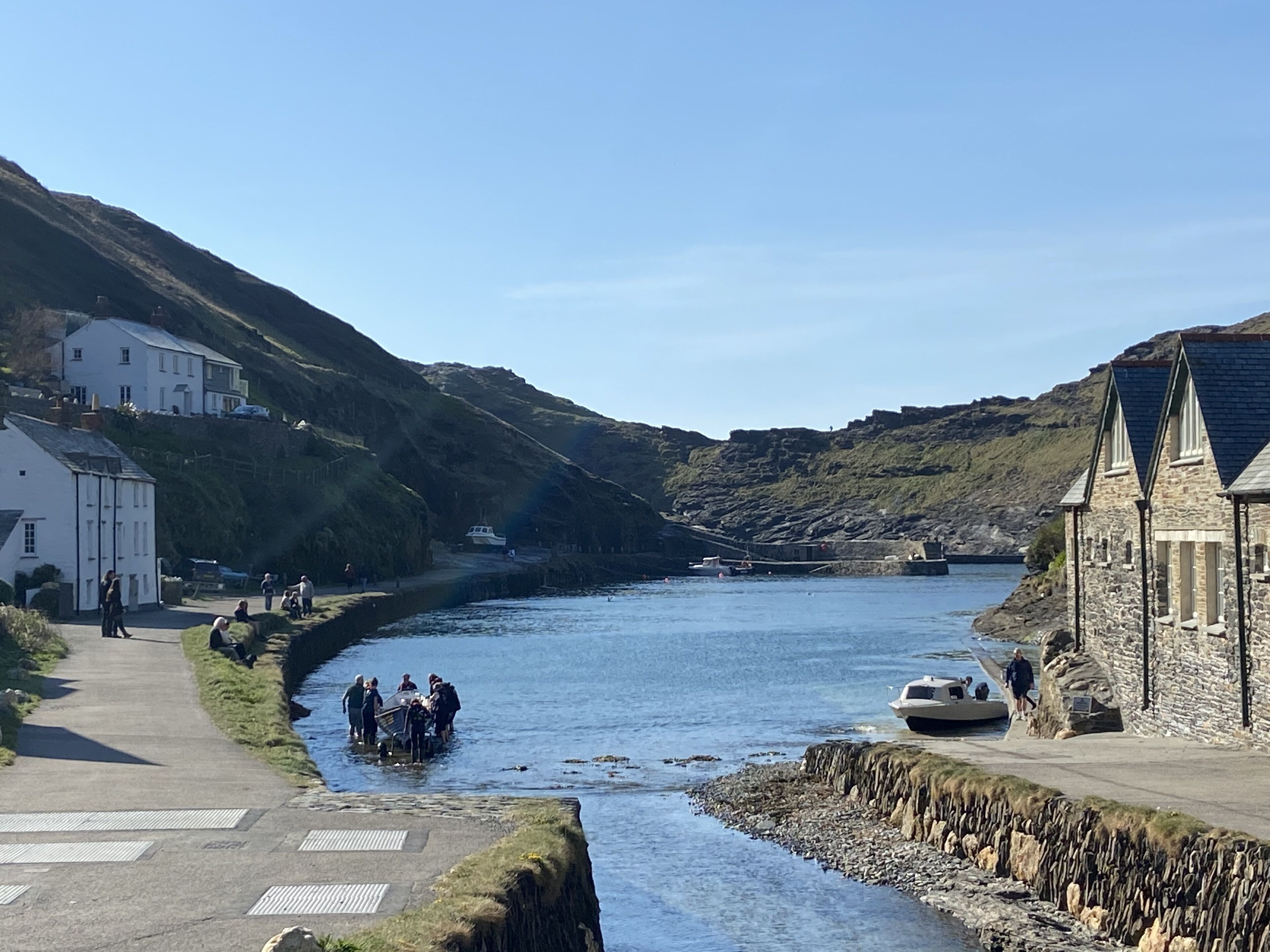 Un pueblo costero con un río estrecho, edificios de piedra y un paseo pavimentado a lo largo de la ribera.