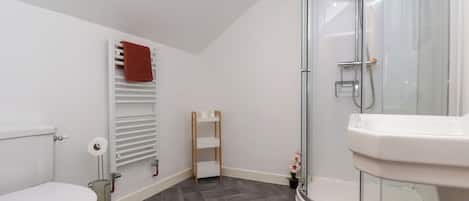 Un baño moderno con inodoro, ducha con cerramiento de vidrio y lavamanos blanco.