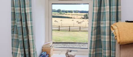 A room with a window overlooking a fenced field with animals.