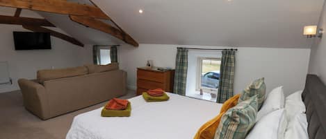 A bedroom with a bed, a sofa, a dresser, a window with curtains, and a television on the wall.